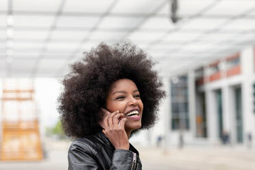 Young woman with afro hair at city train station, making smartphone call - CUF51466