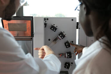Junge Wissenschaftlerinnen und Wissenschaftler betrachten wissenschaftliche Geräte in einem Labor, Blick über die Schulter - CUF51563