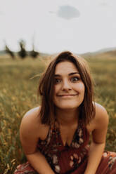 Young woman sitting in field of long grass pulling a face, portrait, Exeter, California, USA - ISF21726