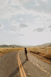 Young barefoot male skateboarder skateboarding on rural road, rear view, Exeter, California, USA - ISF21729