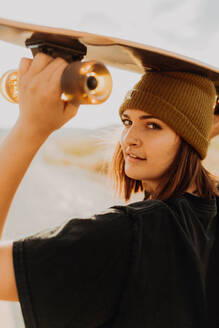 Junge Frau mit Skateboard auf dem Kopf auf einer Landstraße, Porträt, Exeter, Kalifornien, USA - ISF21730