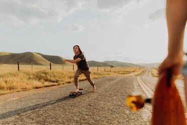 Young barefoot male skateboarder skateboarding on rural road, girlfriend watching, Exeter, California, USA - ISF21734