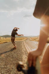 Young barefoot male skateboarder skateboarding on rural road, girlfriend watching, Exeter, California, USA - ISF21735