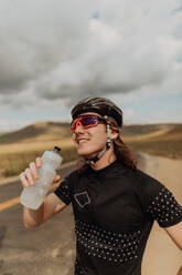 Young male cyclist holding water bottle on rural road, Exeter, California, USA - ISF21762