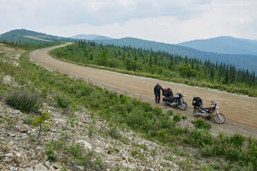 Älterer männlicher Motorradfahrer auf ländlicher Bergstraße mit Motorrad, Hochwinkelporträt, Dawson Creek, Kanada - ISF21801