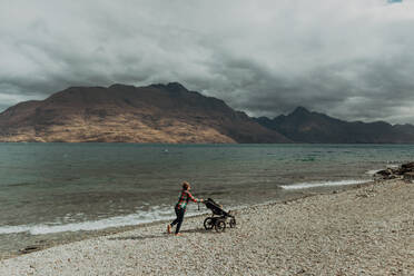 Mutter mit Baby im Kinderwagen beim Spaziergang am Strand, Queenstown, Canterbury, Neuseeland - ISF21819