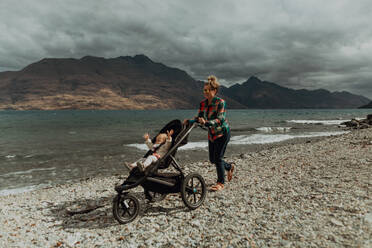 Mutter mit Baby im Kinderwagen beim Spaziergang am Strand, Queenstown, Canterbury, Neuseeland - ISF21820