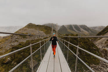 Hiker crossing suspension bridge, Wanaka, Taranaki, New Zealand - ISF21867