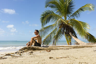 Mann sitzt an einem tropischen Strand, Cahuita Nationla Park, Costa Rica - MAUF02605