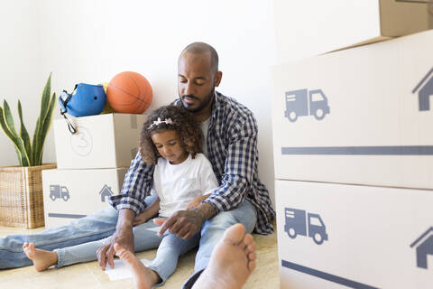 Vater und Tochter sitzen in ihrem neuen Zuhause auf dem Boden, umgeben von Kartons, lizenzfreies Stockfoto