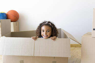 Portrait of happy girl looking out of cardboard box at new home - JPTF00180