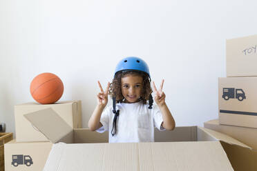 Portrait of girl wearing bicycle helmet looking out of cardboard box at new home - JPTF00181