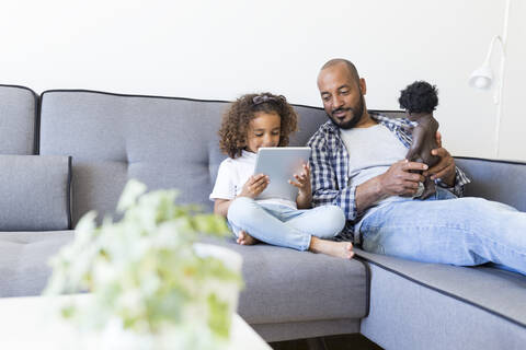 Father and daughter sitting on couch at home with doll and tablet stock photo