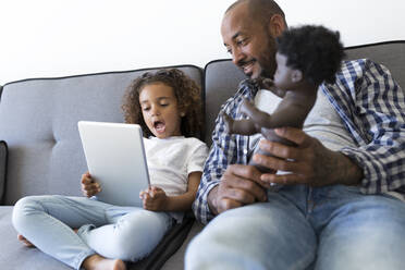 Vater und aufgeregte Tochter sitzen zu Hause auf der Couch und schauen auf ein Tablet - JPTF00186