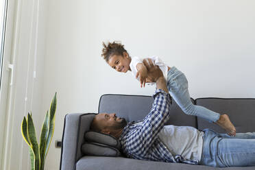 Happy father and daughter playing on couch at home - JPTF00197