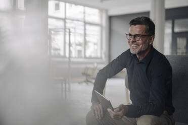 Lächelnder reifer Geschäftsmann mit Tablet und Blick zur Seite - KNSF06063