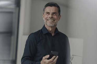 Porträt eines glücklichen reifen Geschäftsmannes, der ein Mobiltelefon hält - KNSF06075