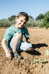 Spanien, Tarragona: Junge schaut in die Kamera, nachdem er im Garten Salat gepflanzt hat - JRFF03391