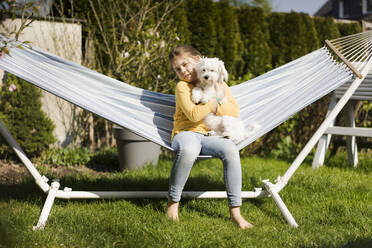 Porträt eines Mädchens mit Hund in einer Hängematte im Garten - MOEF02270