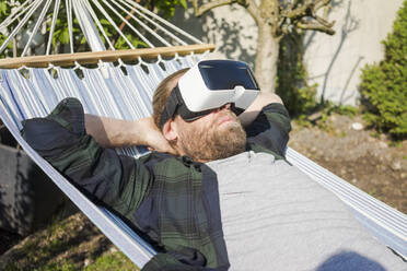 Mann liegt in Hängematte im Garten und trägt VR-Brille - MOEF02276