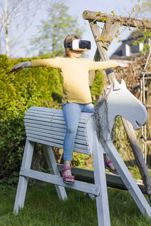 Mädchen übt auf Holzpferd im Garten mit VR-Brille - MOEF02285