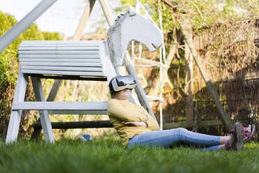 Mädchen sitzt im Garten neben einem Holzpferd und trägt eine VR-Brille - MOEF02286