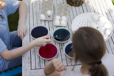 Two girls dyeing Easter eggs on garden table - MOEF02287