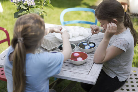 Zwei Mädchen färben Ostereier auf dem Gartentisch, lizenzfreies Stockfoto