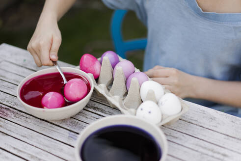 Close-up of girl dyeing Easter eggs in garden - MOEF02297