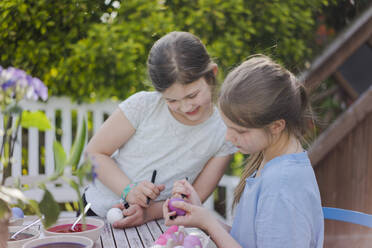 Two girls painting Easter eggs on garden table - MOEF02305