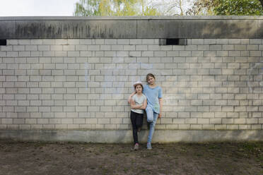 Portrait of two girls standing at a brick wall - MOEF02307