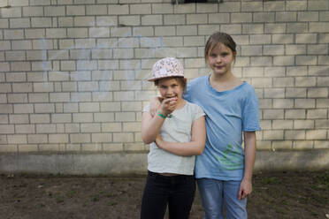 Portrait of two girls standing in front of a brick wall - MOEF02308