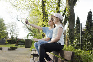 Zwei Mädchen sitzen auf einer Parkbank und machen ein Selfie - MOEF02310