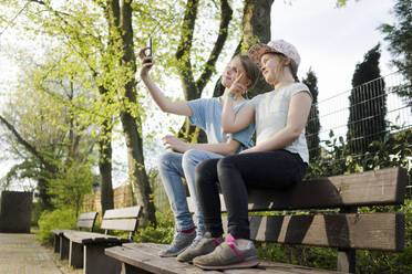 Two girls sitting on a park bench taking a selfie - MOEF02311