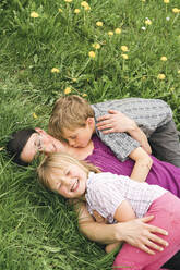 Mother with two children lying on meadow in the countryside - FBAF00764