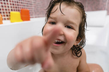 Porträt eines lachenden kleinen Mädchens in der Badewanne, das auf den Betrachter zeigt - MGIF00540