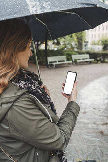 Junge Frau benutzt Handy an einem regnerischen Tag - FBAF00774