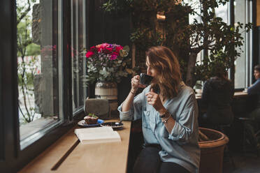 Junge Frau trinkt aus einer Kaffeetasse in einem Café - FBAF00781