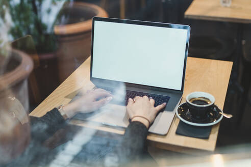 Nahaufnahme einer Frau mit Laptop auf einem Tisch in einem Café - FBAF00790