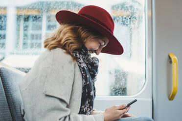 Glückliche junge Frau benutzt Handy in einer Straßenbahn - FBAF00793
