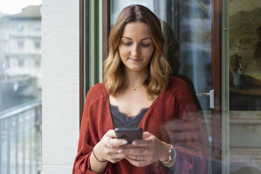 Young woman using cell phone at the balcony door - FBAF00796