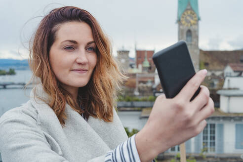 Junge Frau fotografiert mit ihrem Smartphone in der Stadt, Zürich, Schweiz - FBAF00804