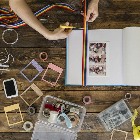 Draufsicht auf die Hände einer Frau, die ein Fotoalbum mit einem Regenbogenband verziert, lizenzfreies Stockfoto