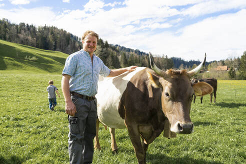 Porträt eines selbstbewussten Landwirts mit Kuh auf der Weide - FBAF00819