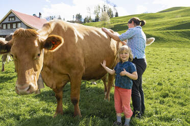 Portrait of girl with mother caring for cow on pasture - FBAF00821