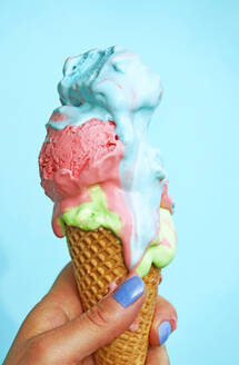 Woman's hand holding ice-cream cone with melting icecream in front of blue background - JTF01251