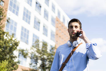 Junger Mann mit Smartphone, Kopfhörer um den Hals in der Stadt - GIOF06515