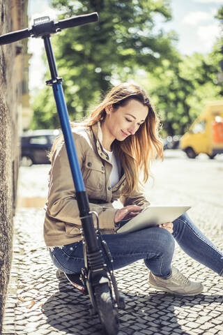 Lächelnde Frau, die auf einem E-Scooter sitzt und ein digitales Tablet benutzt, lizenzfreies Stockfoto