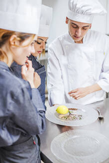 Jungkoch zeigt sein vorbereitetes Dessert auf einem Teller - LJF00183