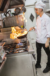 Jungkoch mit Flammenpfanne in traditioneller spanischer Restaurantküche - LJF00199